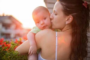 Mother holds and kisses her baby on the cheek.