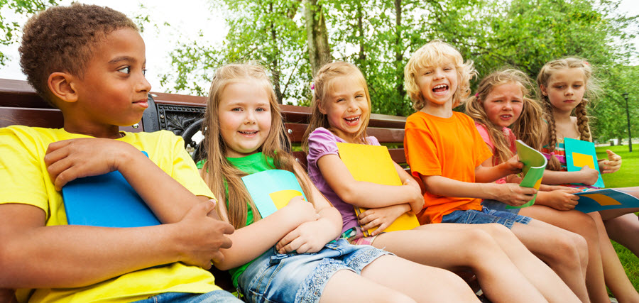 School kids sitting in a row on a bench outside