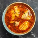 A bowl of soup. It has tomatoes, chicken and potatoes.