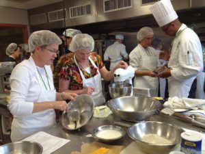 Multiple people in aprons and hairnets baking around a kitchen island. 