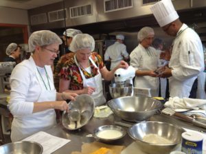 Multiple people in aprons and hairnets baking around a kitchen island.