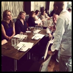 Chef Mehta talking to everyone sitting at the table, including Alice Bast.