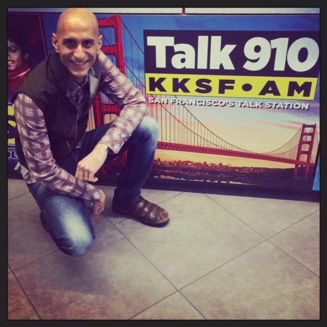Chef Mehta kneeling by a poster that says "Talk 910"