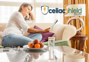 A woman sits on a beige sofa reading a booklet. There is fruit, a glass of water, and a lamp on a glass coffee table. The text “celiacShield Study” with a shield logo appears in the top right corner.