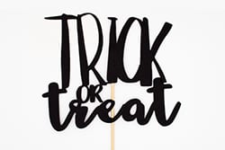 Black cutout sign with the words Trick or Treat in bold, playful font on a white background, attached to a thin wooden stick.