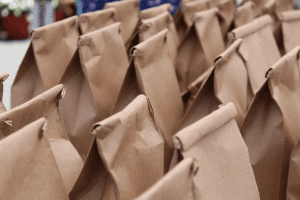 A group of brown paper bags, each rolled closed at the top, stands in neat rows. The bags appear identical and are arranged close together, suggesting preparation for an event or distribution.