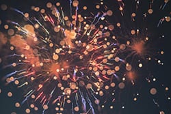 Bright orange and gold fireworks burst in the night sky, with scattered blurred light spots and streaks radiating outward from the center.