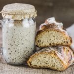 A loaf of sourdough bread next to a jar of mature sourdough starter.