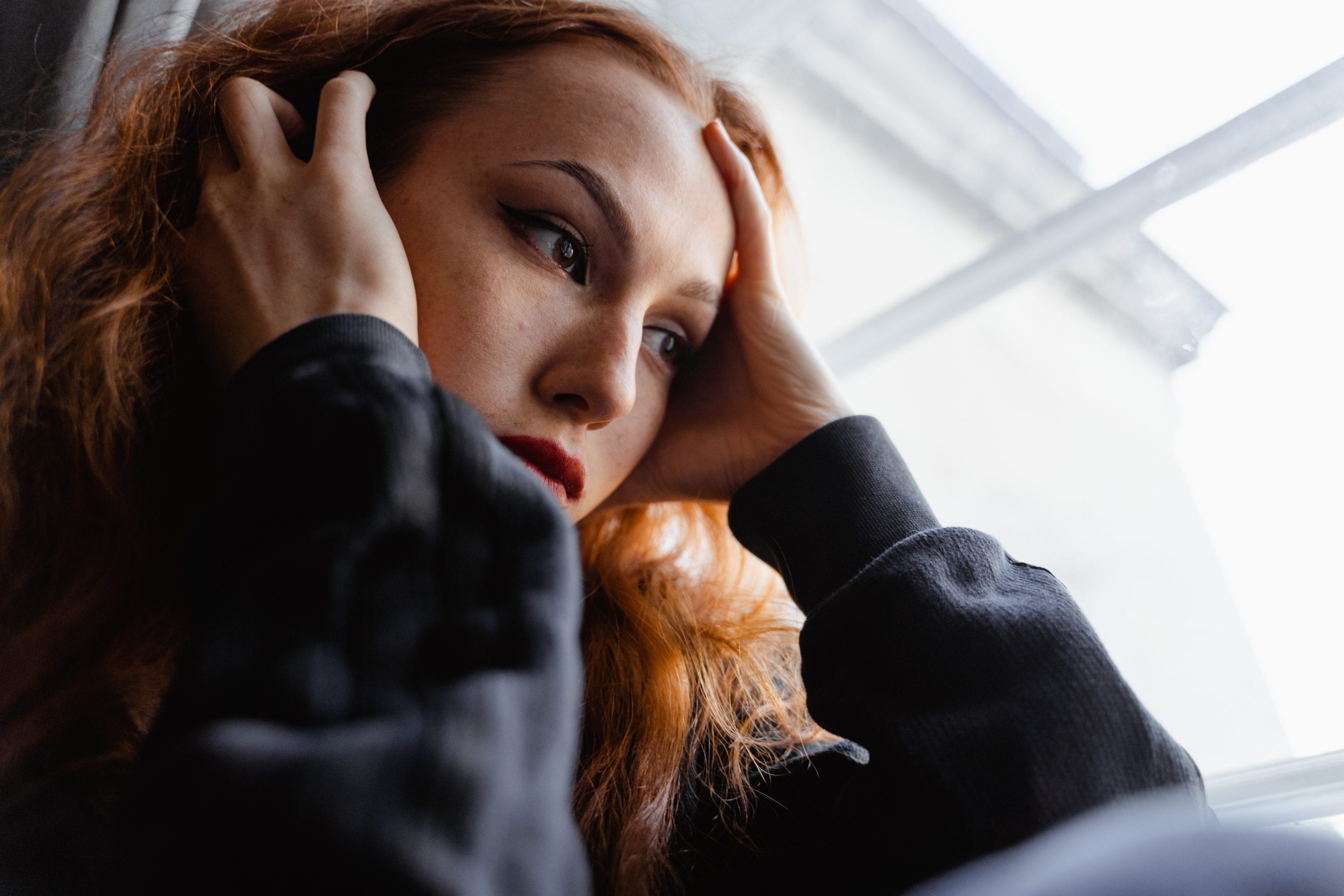 Woman with her head in her hands looking out a window. 