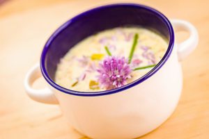 A small bowl of corn chowder with a purple flower on top as garnish. 