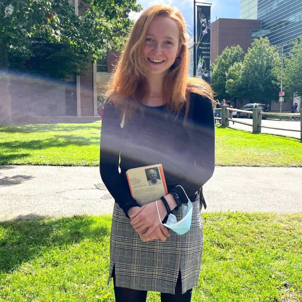 Evie is standing outside with a book in her hands, smiling in the sun.