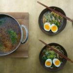 Two bowls of miso ramen next to pot of broth.