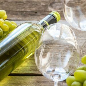 An empty wine glass lying next to a wine bottle and white (green) grapes.