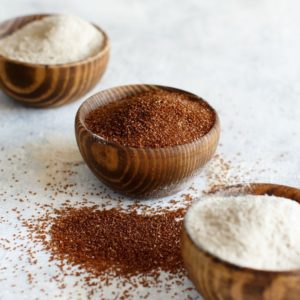 A bowl of teff seeds in between two bowls of teff flour.