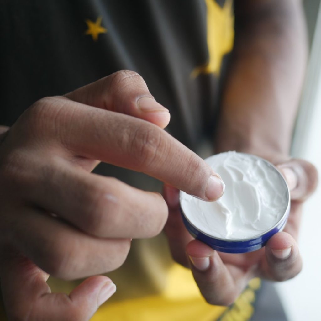 A hand reaching into a small tin of cream.