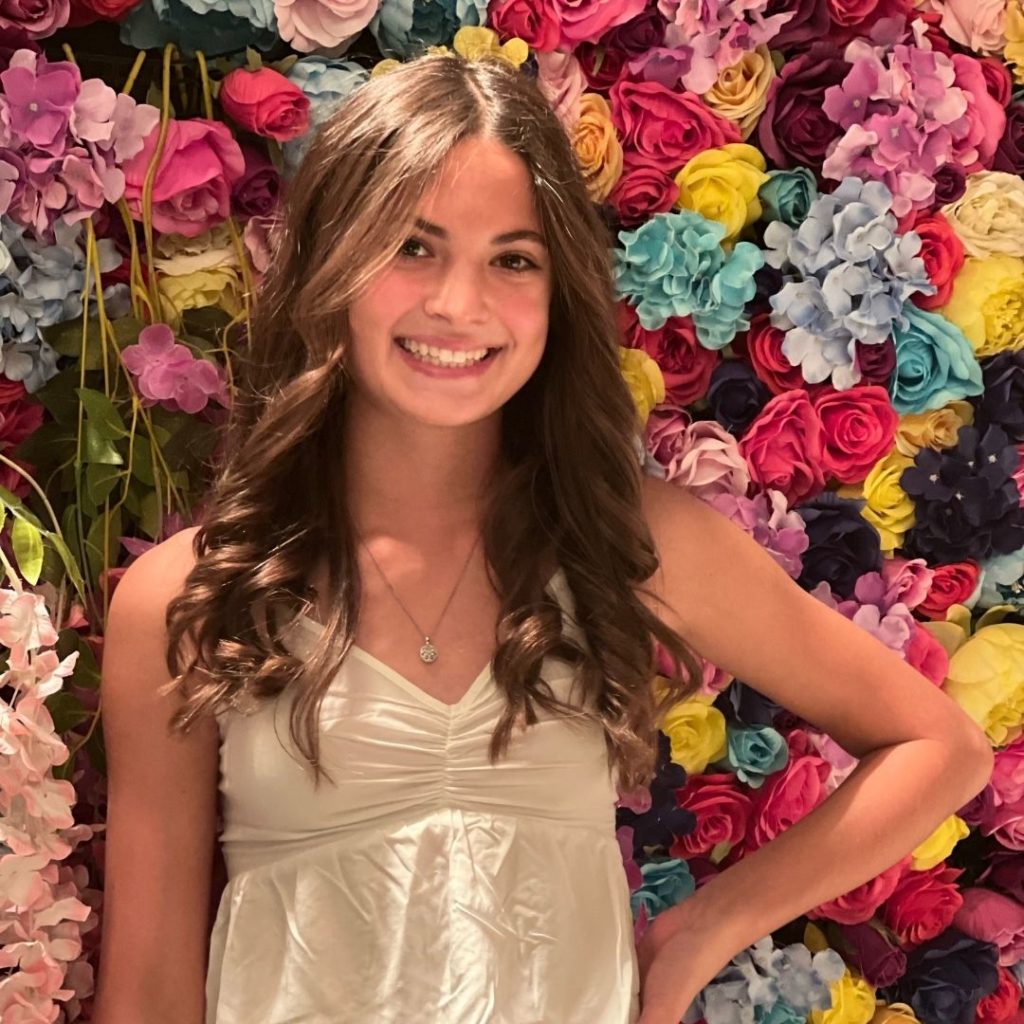 A photo of Kenzie standing in front of a wall of flowers.