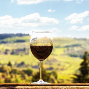 A glass of Chianti wine on a table in front of the Italian countryside.