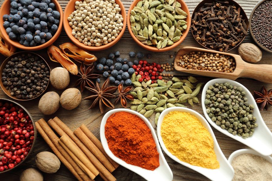 Bowls and spoons full of different spices sit on a table.