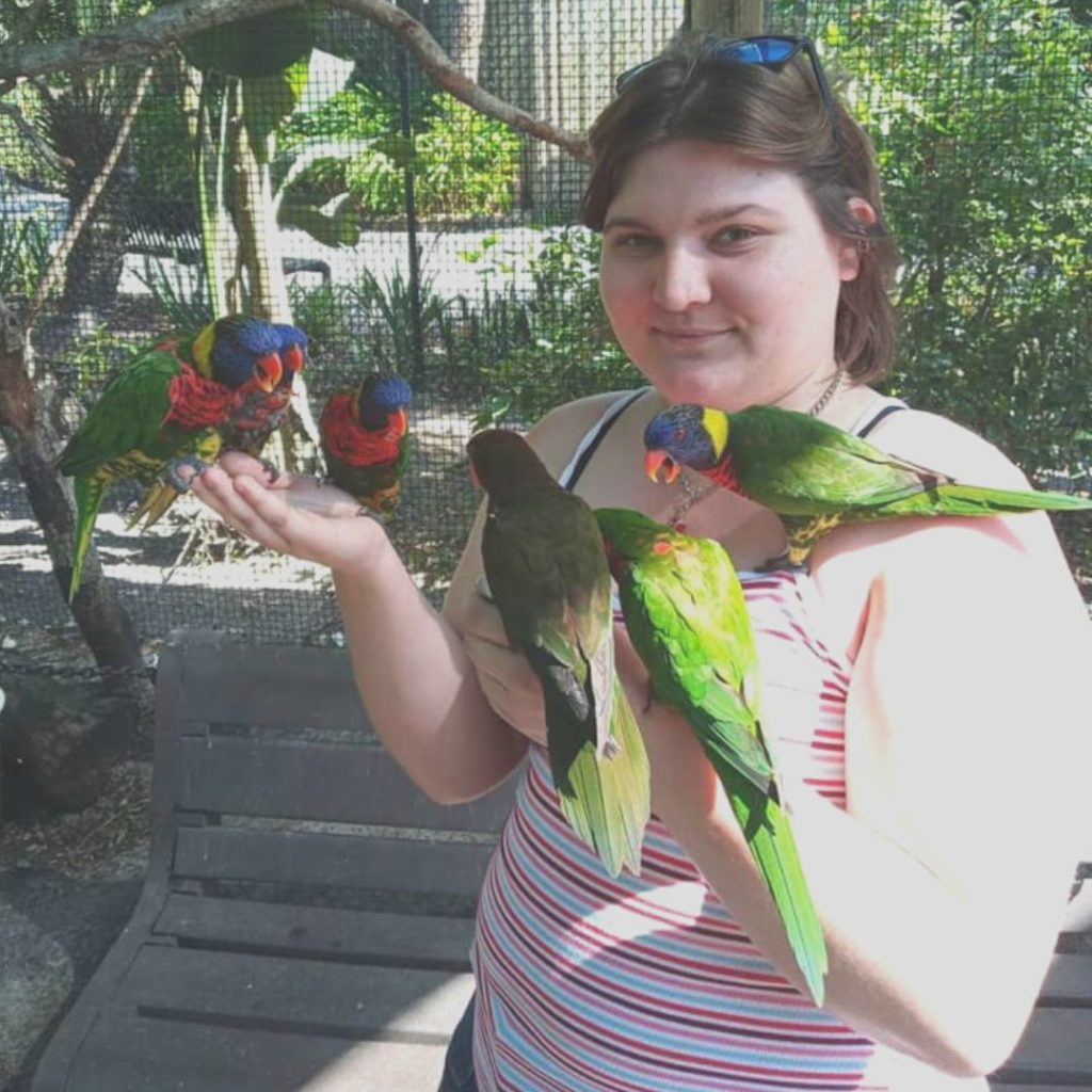 A photo of Alia. Colorful birds are perched on her fingers.