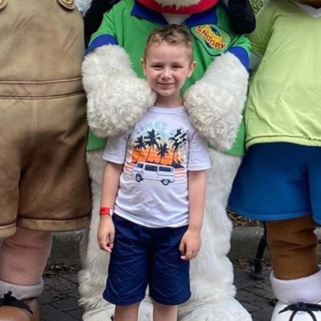 A photo of Landon with mascots. He is smiling.