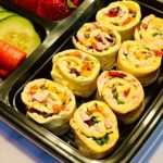 A lunchbox with the pinwheels, cucumbers, and strawberries.