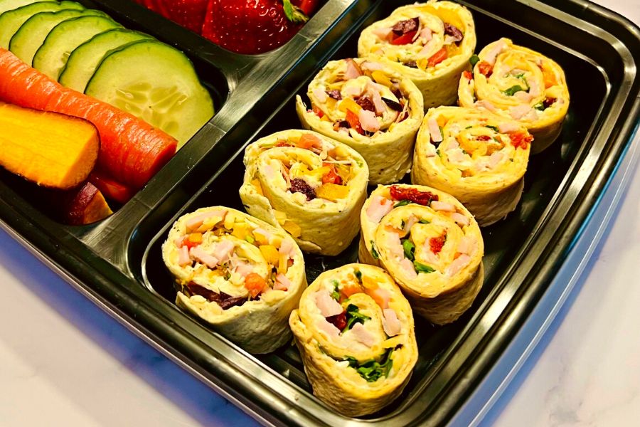 A lunchbox with the pinwheels, cucumbers, and strawberries.