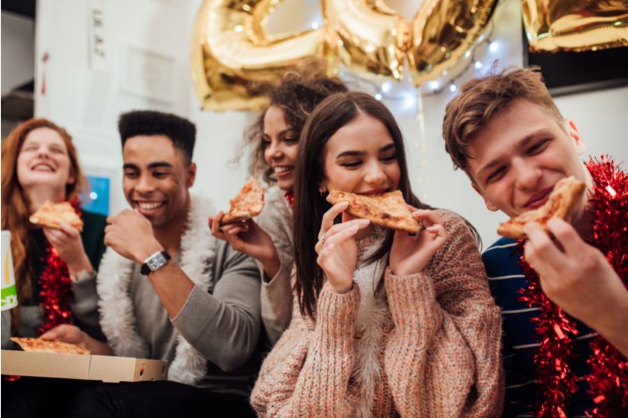 Teenagers eating pizza together, smiling. 