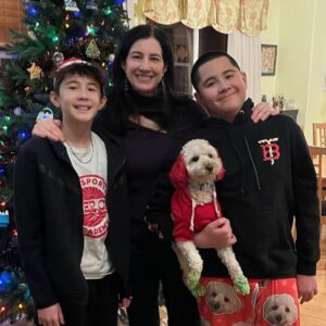 A photo of Renzo, Weslan, Corine and their dog smiling in front of a Christmas tree.