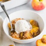 A bowl of peach crisp topped with ice cream.