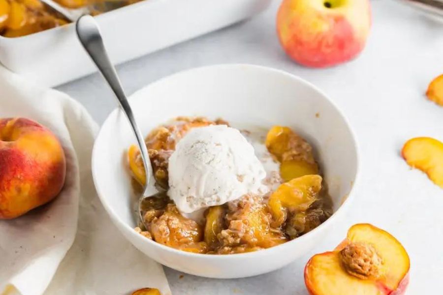 A bowl of peach crisp topped with ice cream.