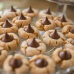 Peanut butter blossom cookies on a serving plate. They are peanut butter cookies with a Hershey's kiss in the middle.