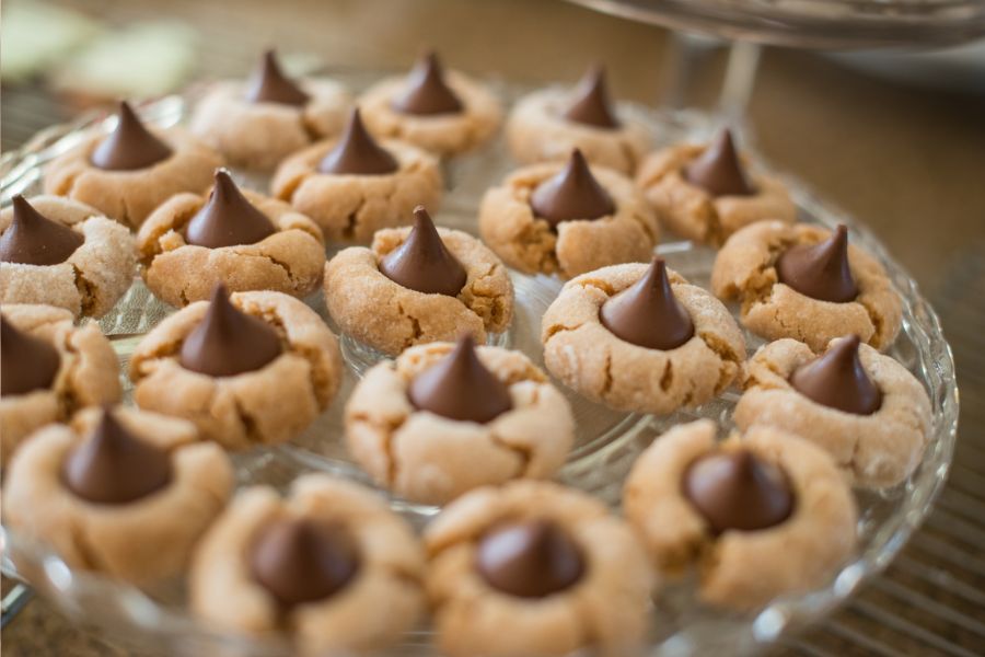 Peanut butter blossom cookies on a serving plate. They are peanut butter cookies with a Hershey's kiss in the middle.