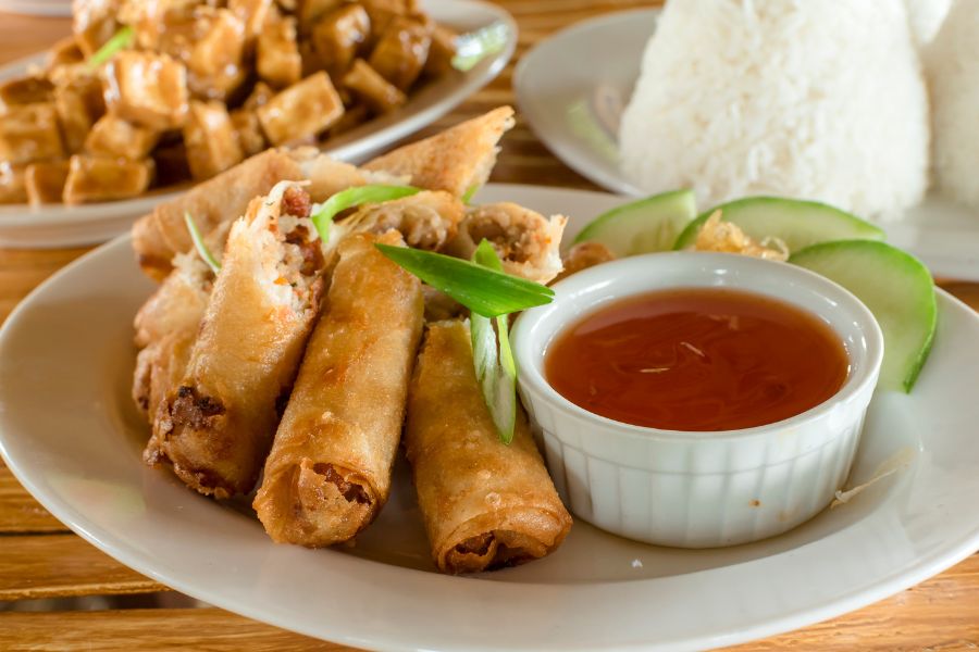 A plate of egg rolls next to a bowl of dipping sauce. 