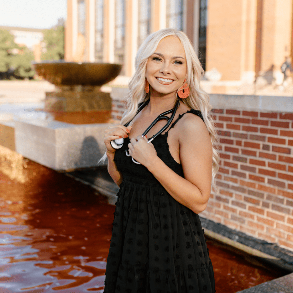 Macy stands in front of a brick wall and water with a stethoscope.