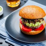A black bean burger on a plate next to a bowl of guacamole.