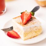 A piece of tres leches cake with strawberry slices.