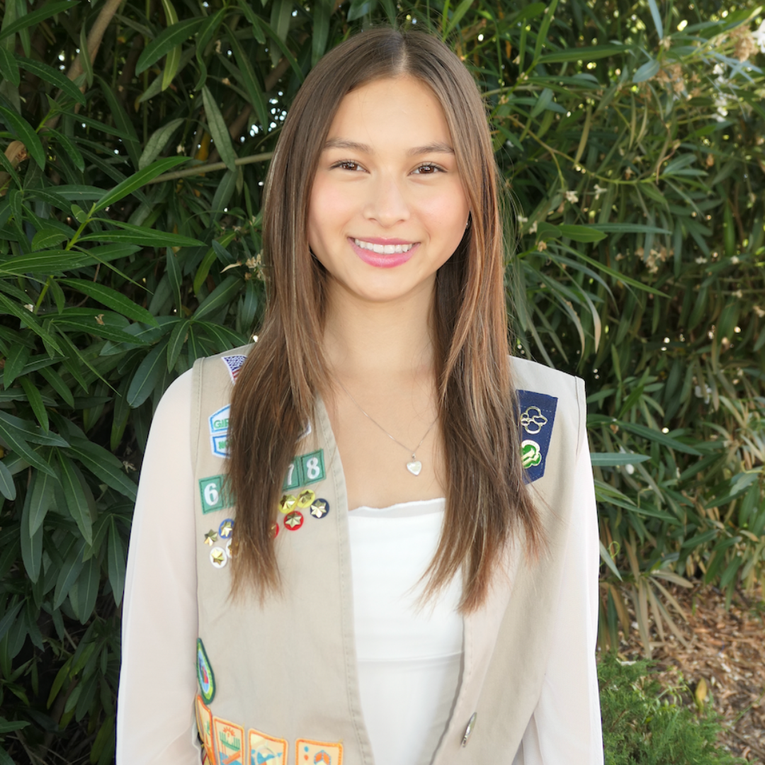 Sophia stands in front of greenery in her girl scout vest