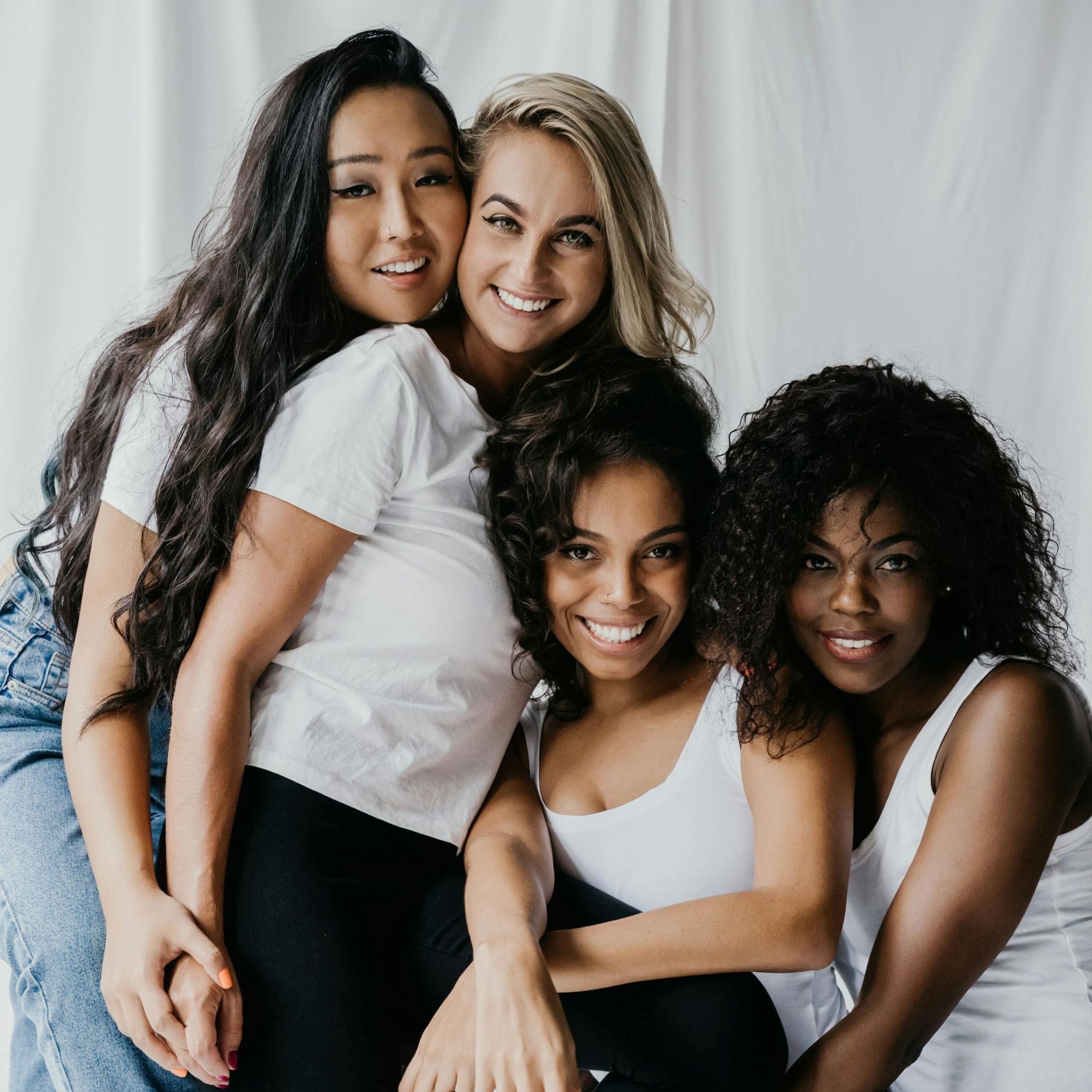 Women of various races and skin tones smile and hug. 