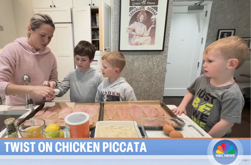 An adult and three young boys stand at a kitchen counter with trays of raw chicken breasts and various cooking ingredients. The adult is preparing food while the children watch. Text reads TWIST ON CHICKEN PICCATA. NBC News logo is visible.