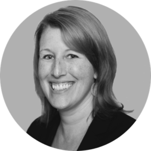 A woman with shoulder-length light brown hair, smiling, wearing a dark blazer and earrings, shown in a grayscale circular portrait against a plain background—reflecting her role in beyond celiac investments.