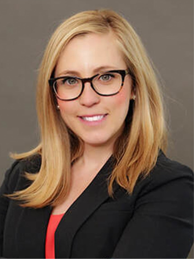 Headshot of a blonde woman wearing glasses and a black blazer.