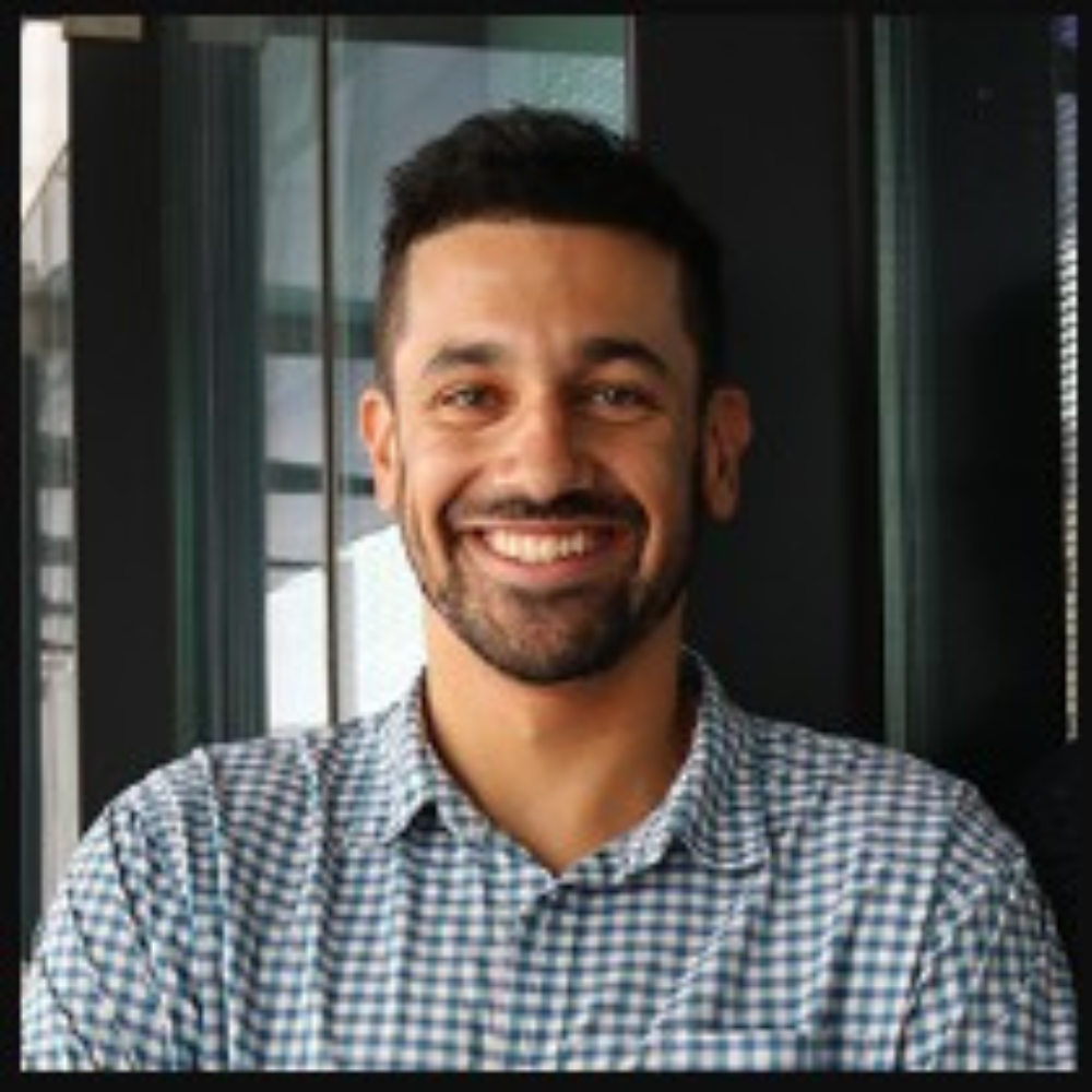 A smiling man with a beard wearing a blue and white checkered shirt.